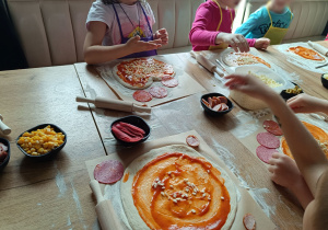 Dzieci nakładają na pizzę wybrane dodatki.