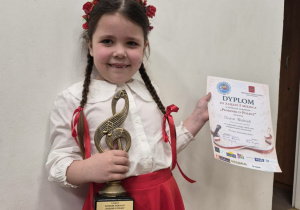 Dziewczynka prezentująca statuetkę i dyplom.